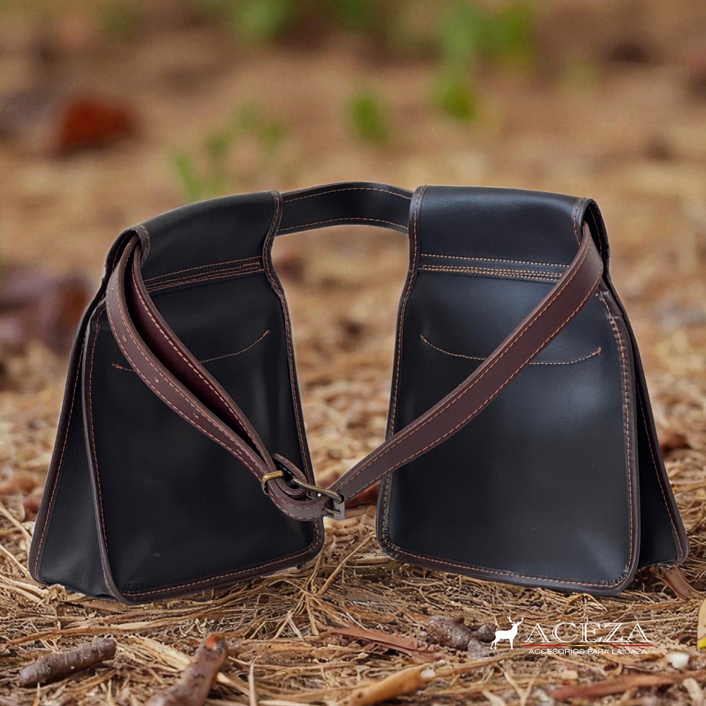 Bolsa de ojeo Aceza en cuero marrón oscuro apoyada sobre el suelo de bosque con pinocha y ramas secas.