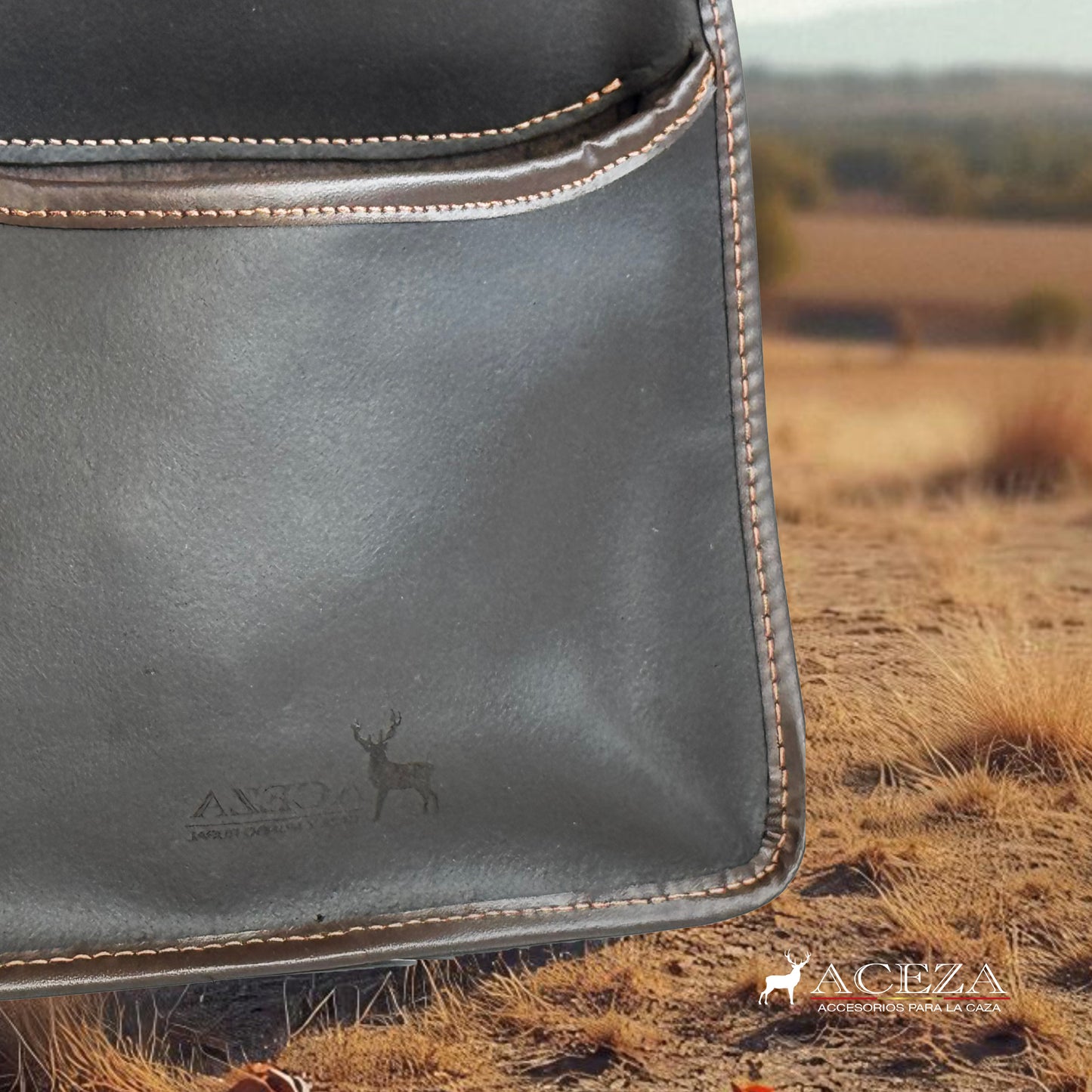 Detalle de la bolsa de ojeo Aceza en cuero marrón oscuro con costuras visibles y logotipo grabado, sobre un paisaje de campo seco y rural al fondo.
